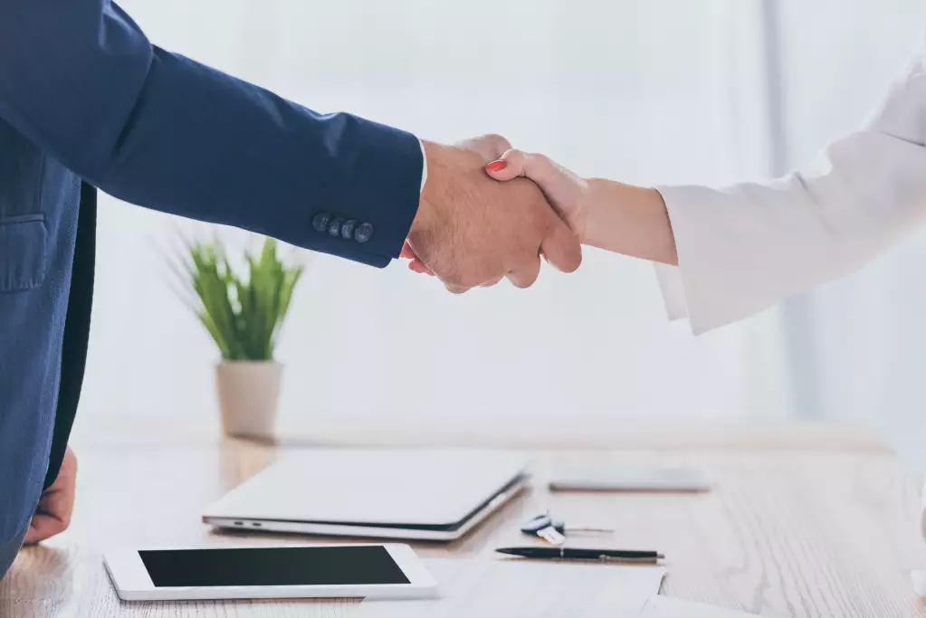 Partial view of businessman shaking hands with woman while sitting at wooden desk